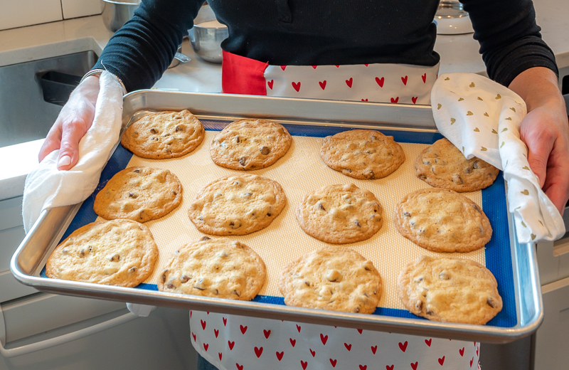 Fresh baked chocolate cookies on a baking sheet, held by a woman.